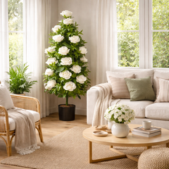 Planta artificiala decorativa cu trandafiri albi 135 cm in ghiveci negru amplasata in coltul unui living modern langa canapea.